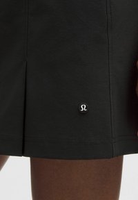 Pantalones cortos deportivos negros de tejido suave, con una abertura lateral y un pequeño logo circular en el dobladillo inferior izquierdo.