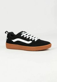 Le sneakers in suede nere presentano una striscia laterale bianca, lacci bianchi e una suola in gomma marrone. Un dettaglio notevole è un piccolo logo sulla linguetta.