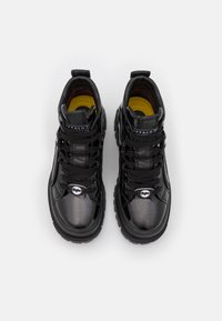 Zapatillas negras tipo botín con acabado brillante, que cuentan con cordones negros, lengüetas acolchadas y plantillas amarillas, diseñadas con una suela gruesa.