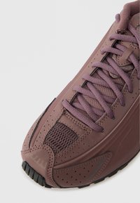 Violet sportbačiai su tekstūruotu sintetiniu paviršiumi, tinklinėmis detalėmis, plokščiais raišteliais ir guminiu padu su taškuotais raštais.