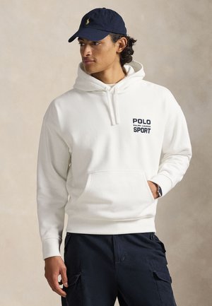 White hooded sweatshirt with a front pocket and "POLO RALPH LAUREN SPORT" printed in black. Worn with navy cargo pants and a dark cap.