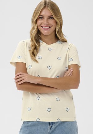 Flødefarvet T-shirt med korte ærmer, der har et mønster af blå omridsede hjerter. Blødt bomuldsmateriale, løs pasform, rund hals.