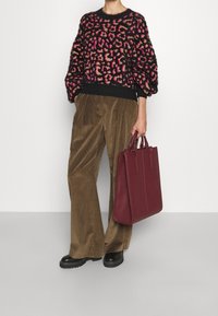 Svart tröja med rosa och beige leopardmönster, vida olivgröna corduroybyxor och en mörkröd läderhandväska. Kraftiga svarta ankelskor.