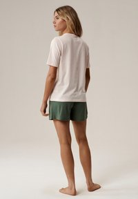 Jasnoróżowa koszulka z krótkim rękawem zestawiona z ciemnozielonymi szortami, wyświetlana z tyłu. Miękki materiał i luźny krój, minimalne wykończenia.