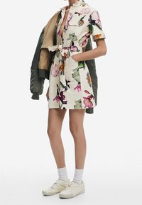 Sukienka w jasnobeżowym kolorze w kwiatowy wzór, z krótkimi rękawami i wiązaniem w talii. Połączona z zieloną kurtką bombową i białymi trampkami z teksturowaną podeszwą.