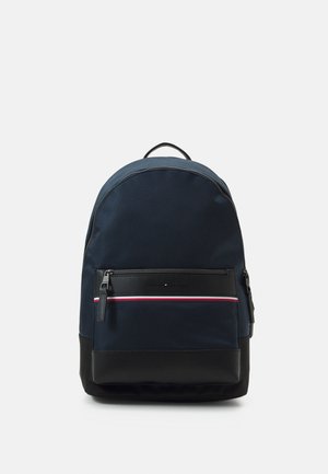 Marineblauwe rugzak met zwarte bodem, voorvak met rits met een rood, wit en blauw streepje, en bovenste draaggreep op een effen achtergrond.