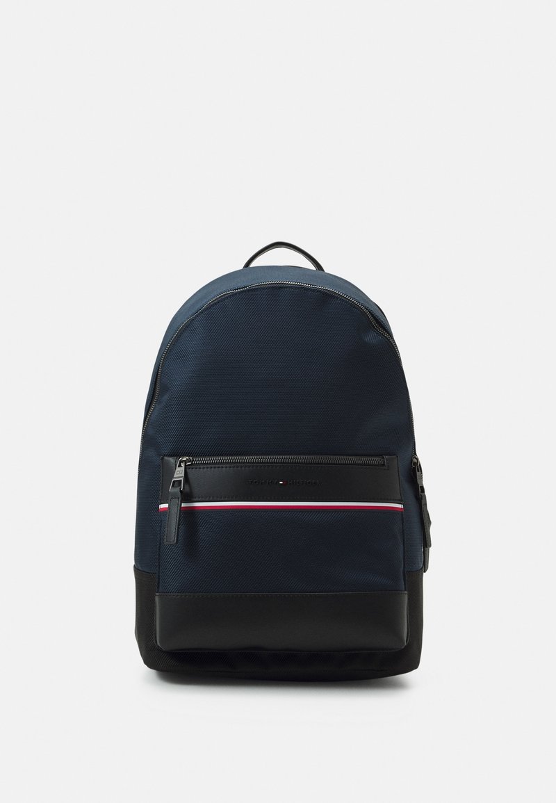 Sac à dos bleu marine avec base noire, poche avant zippée présentant une bande rouge, blanche et bleue, et poignée de transport supérieure sur fond uni.