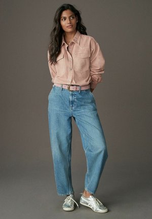 Lichtroze, knoopsluiting corduroyshirt met twee borstzakken, gecombineerd met hooggerokte, losse blauwe denim jeans en zilveren sneakers.