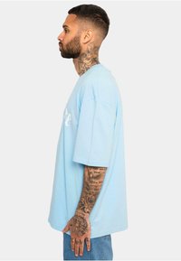 Lysblå oversized t-shirt med korte ærmer, der har en rund halsudskæring og hvid tekst trykt på forsiden.