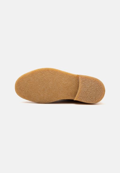 Semelle de chaussure en caoutchouc crêpé marron clair avec une surface plate texturée et un petit talon sur fond uni.