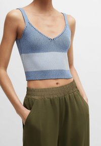 Světle modrý žebrovaný crop top se vzhledem do V a vodorovným bílým pruhem v pase. V kombinaci s olivově zelenými kalhotami s elastickým pasem.
