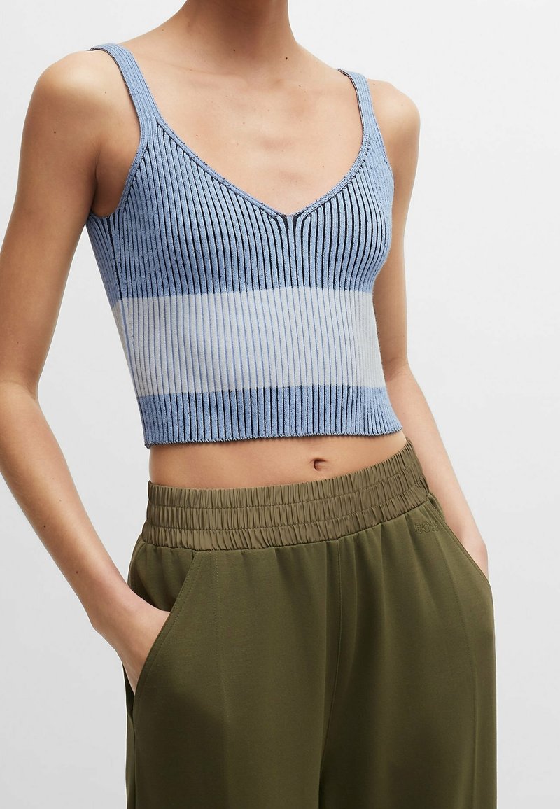 Světle modrý žebrovaný crop top se vzhledem do V a vodorovným bílým pruhem v pase. V kombinaci s olivově zelenými kalhotami s elastickým pasem.