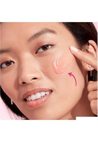 En klar gelkräm applicerad på en kind, med ett finger som pekar på den. Produkten är ljusrosa med en slät textur på solbrun hud.