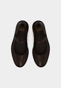 Σκούρα καφέ δερμάτινα παπούτσια Mary Jane με λουριά και αγκράφες, στρογγυλεμένες μύτες και επώνυμα πάτοι με τη λέξη "BRONX" σε λευκό φόντο.