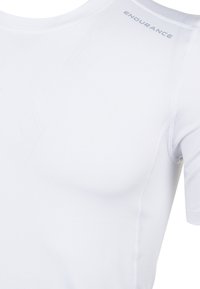 Vit atletisk t-shirt i ett glatt och stretchigt tyg. Har korta ärmar, en rund halsringning och en diskret logotyp på axeln.