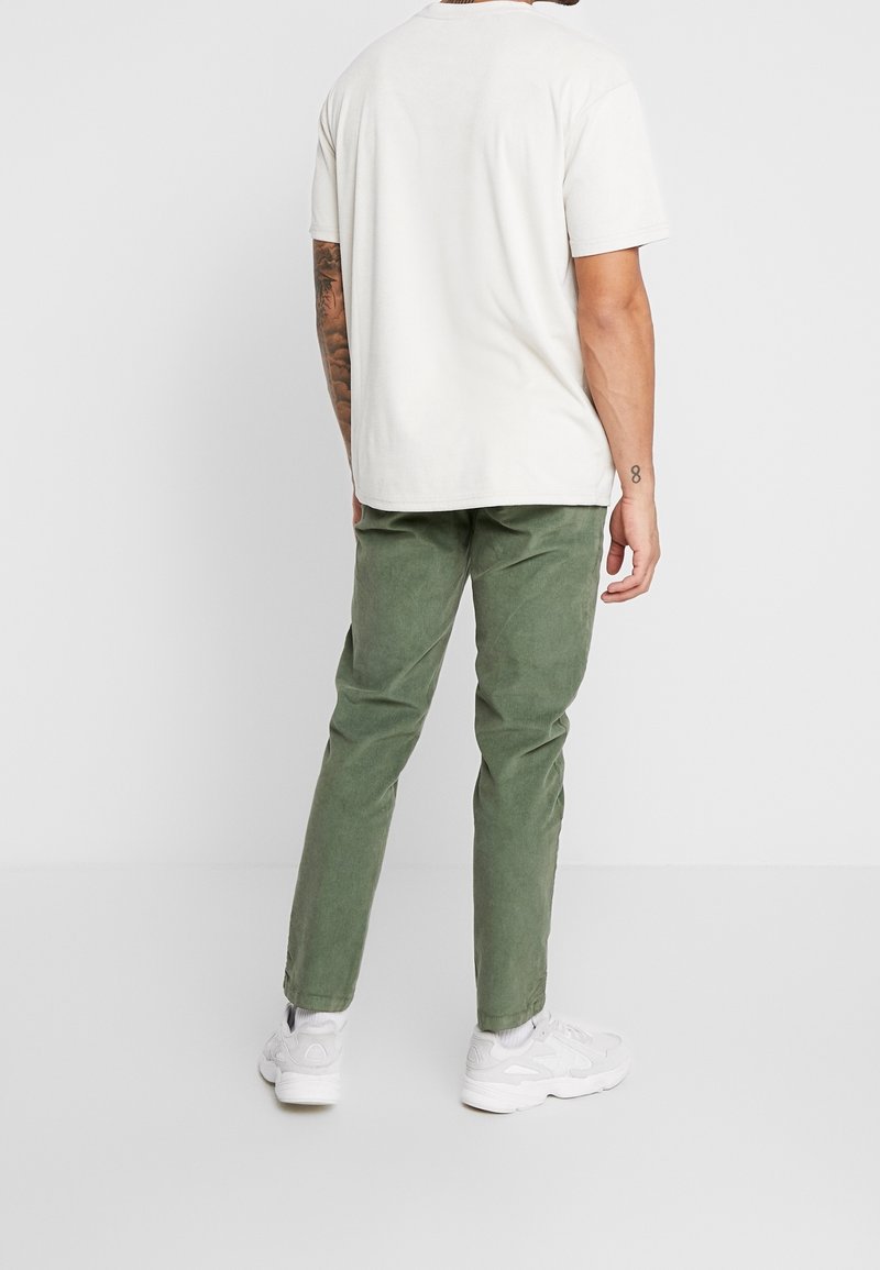 Witte korte mouwen t-shirt gecombineerd met groene corduroy broek. De broek heeft een rechte pasvorm en wordt aangevuld met witte sneakers.