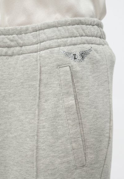 Sivé teplákové nohavice s hladkou textúrou, ozdobené malým detailom v podobe krídel z trblietavých kamienkov a vybavené bočnými vreckami pre praktickosť.