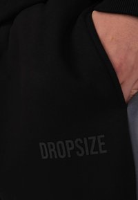 Czarne dresy z kieszenią, z napisem "DROPSIZE" w subtelnym, matowym wykończeniu. Miękka faktura, casualowy design, elastyczny pas.