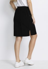 Falda negra hasta la rodilla hecha de algodón, con cintura elástica y una abertura lateral, combinada con zapatillas blancas. Diseño sencillo y color sólido.