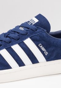 Blue suede sneaker with white three stripes, “CAMPUS” text, and round toe. Features textured laces and a white rubber sole.