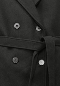 Double-breasted black coat in soft fabric, featuring black buttons and a matching tie belt. Includes a notched collar and smooth texture.