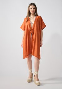 Cubierta naranja hasta la rodilla hecha de tela ligera, con cuello en v, mangas cortas y un detalle de lazo en la cintura.