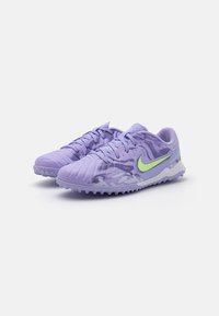 Nike fotballsko i lys lilla med en teksturert overflate, grønn aksentlogo og formede pigger for godt grep på kunstgress.