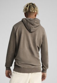 Sudadera marrón con capucha y cordones, puños y dobladillo acanalados. Textura suave, corte relajado, costuras visibles y sin patrones ni logos.