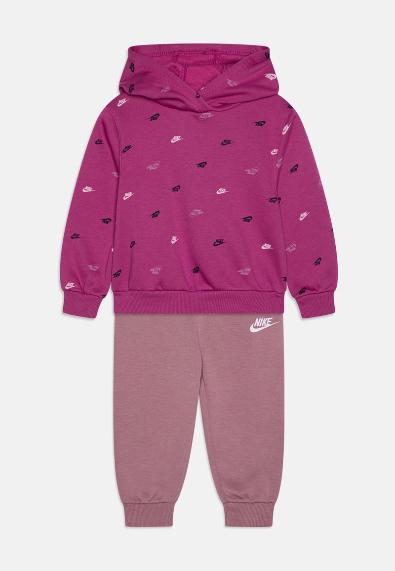 Felpa rosa con loghi Nike neri, bianchi e grigi sparsi; abbinata a pantaloni della tuta rosa coordinati con un logo Nike bianco sulla gamba.