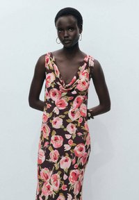 Rochie florală cu decolteu în formă de cowl, având trandafiri mari roz și piersici pe un fundal maro închis. Design fără mâneci cu o siluetă ajustată.