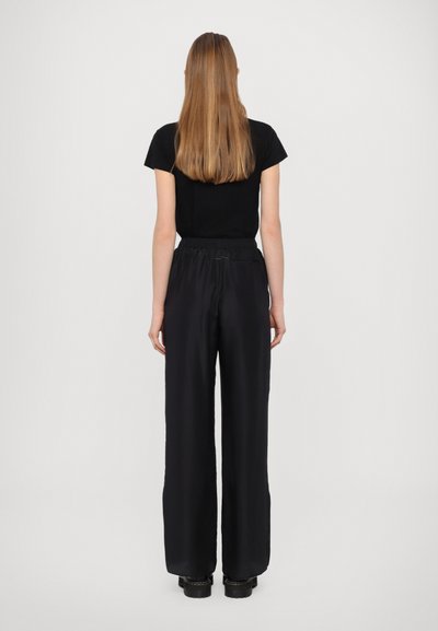Black t-shirt and wide-leg black pants, with an elastic waistband, shown from the back against a light gray background.