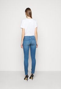 Jeans ajustados azul con una cintura de altura media, que cuentan con un diseño de 5 bolsillos y una textura de denim suave, combinados con una camiseta blanca básica.