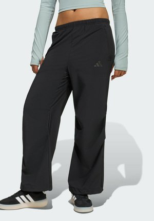 Mustat urheiluhousut, joissa on löysä istuvuus, joustava vyötärönauha ja hillitty Adidas-logon yksityiskohta. Materiaali vaikuttaa sileältä ja kevyeltä.