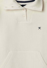 Krémová polo košile s vroubkovaným límcem, tříknoflíkovou légou a vyšitým logem na hrudi; má přední kapsu.