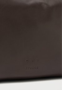 Geantă maro din piele, cu o textură netedă, logo-ul brandului "CPH STUDIOS" embosat și un design minimalist.