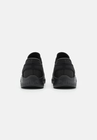 Fekete sportcipők sima textil felsőrésszel, strukturált sarokkal és gumitalppal. Slip-on kialakítással és lekerekített orral rendelkezik.