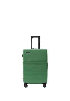 Zielona walizka na kółkach z twardą obudową, czterema czarnymi kołami i wysuniętą czarną teleskopową rączką, pokazana na białym tle.