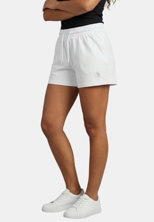 Woman wearing white elastic-waist shorts with drawstring and white sneakers, standing with arms crossed against white background.