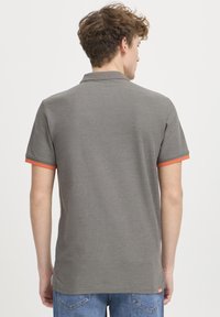 Grå polo skjorte med korte ærmer, med orange detaljer på manchetterne. Tekstureret stof, klassisk krave og etiketdetalje i siden synlig.