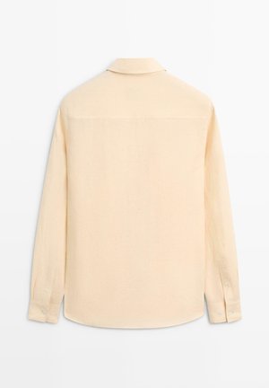 Beige langærmet skjorte med knappede manchetter, krave og lige kant, vist bagfra på en ensfarvet hvid baggrund.