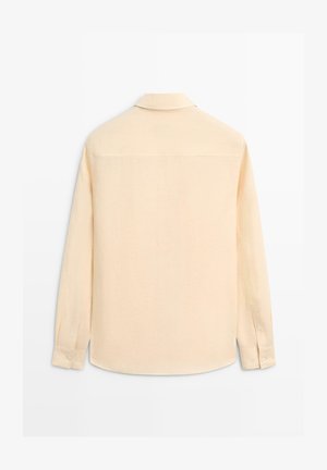 Beżowa koszula z długim rękawem, zapinanymi mankietami, kołnierzykiem i prostym dołem, pokazana od tyłu na białym, jednolitym tle.