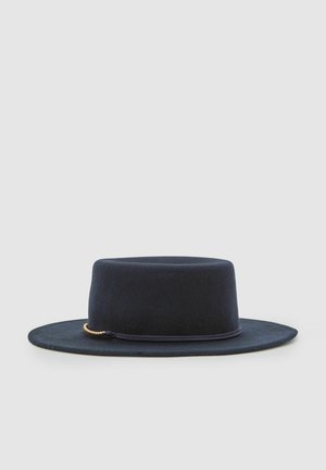 Cappello di feltro nero con tesa larga e corona piatta. Presenta un dettaglio decorativo con catena in tono oro. Texture liscia e forma strutturata.