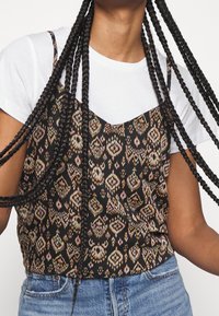 Haut caraco noir à motifs géométriques en rose, orange et crème. Présente des bretelles fines et un décolleté en V, superposé à un t-shirt blanc.