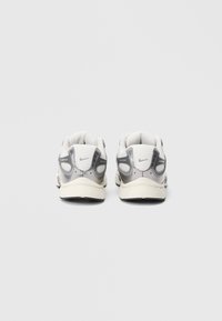 Λευκά και γκρι αθλητικά παπούτσια από υλικά διχτυού και συνθετικά, με χαρακτηριστικές λεπτομέρειες στο πίσω μέρος και υφασμένες σόλες για καλύτερη πρόσφυση.