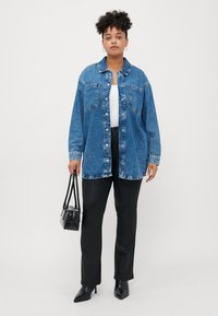 Denim button-up shirt, blue with light wash accents, two front pockets, paired with black straight-leg pants and a small black bag.