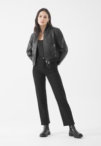 Giacca bomber nera in pelle con polsini a coste, abbinata a pantaloni neri a vita alta e stivali neri alla caviglia. Design minimalista, finitura elegante.