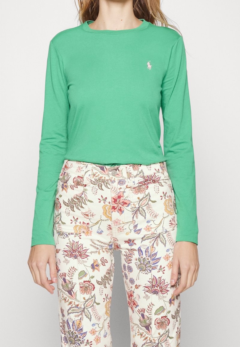 Camiseta de manga larga verde de algodón con cuello redondo y un pequeño logo. Combinada con pantalones crema de estampado floral, que presentan flores multicolores.