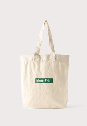 Beige draagtas met twee handvatten en een groen tekstlabel met de tekst "Mon-Fri:" gecentreerd aan de voorkant tegen een effen lichte achtergrond.