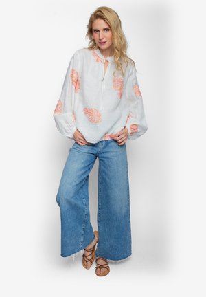 Biała lniana bluzka z pomarańczowymi wzorami liści, luźny krój, dekolt z rozcięciem; w połączeniu z niebieskimi szerokimi spodniami dżinsowymi i brązowymi sandałami na paski.