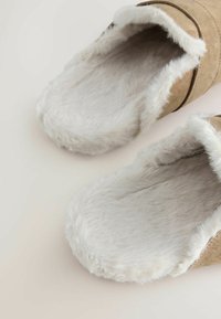 Bruine suède slippers met een pluizige witte voering en bontafwerking. Open ontwerp met een zachte textuur en een gebogen vorm voor comfort.